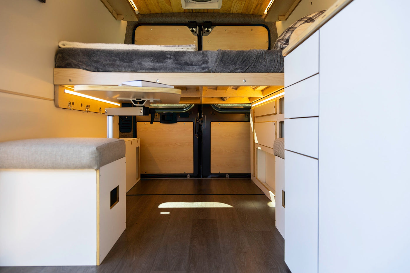 Explore this modern RV rental interior featuring a comfy elevated bed, flexible table, and smart storage solutions. — photo 19
