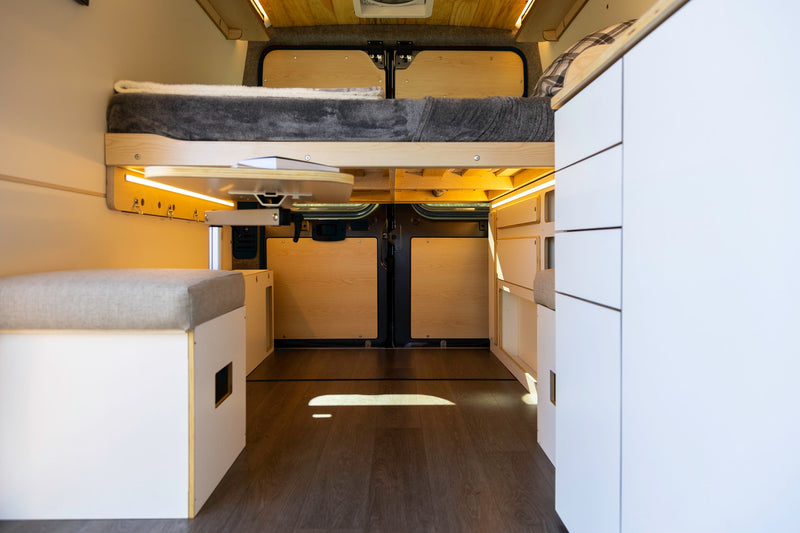 Explore this modern RV rental interior featuring a comfy elevated bed, flexible table, and smart storage solutions. — photo 19