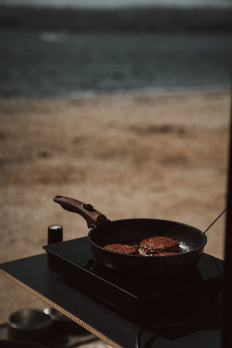 Sizzling patties on a portable stove, a tasty meal during your RV rental trip. Scenic outdoor cooking with a view.