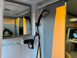 Compact RV rental shower with black handheld shower head, faucet, and mirror, featuring an odor control system.