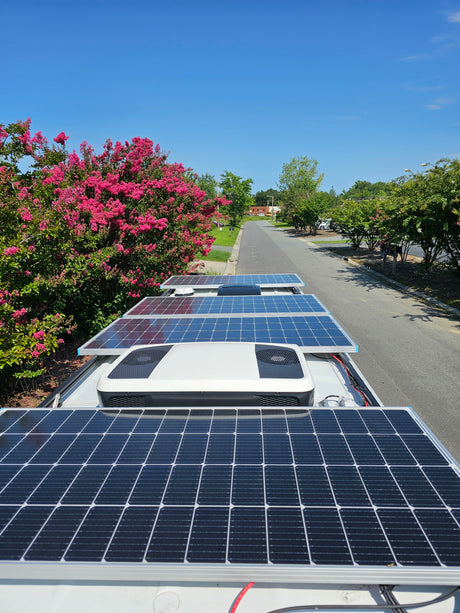 View from an RV rental rooftop: solar panels, AC unit, and a vibrant street scene with pink trees under a clear sky.