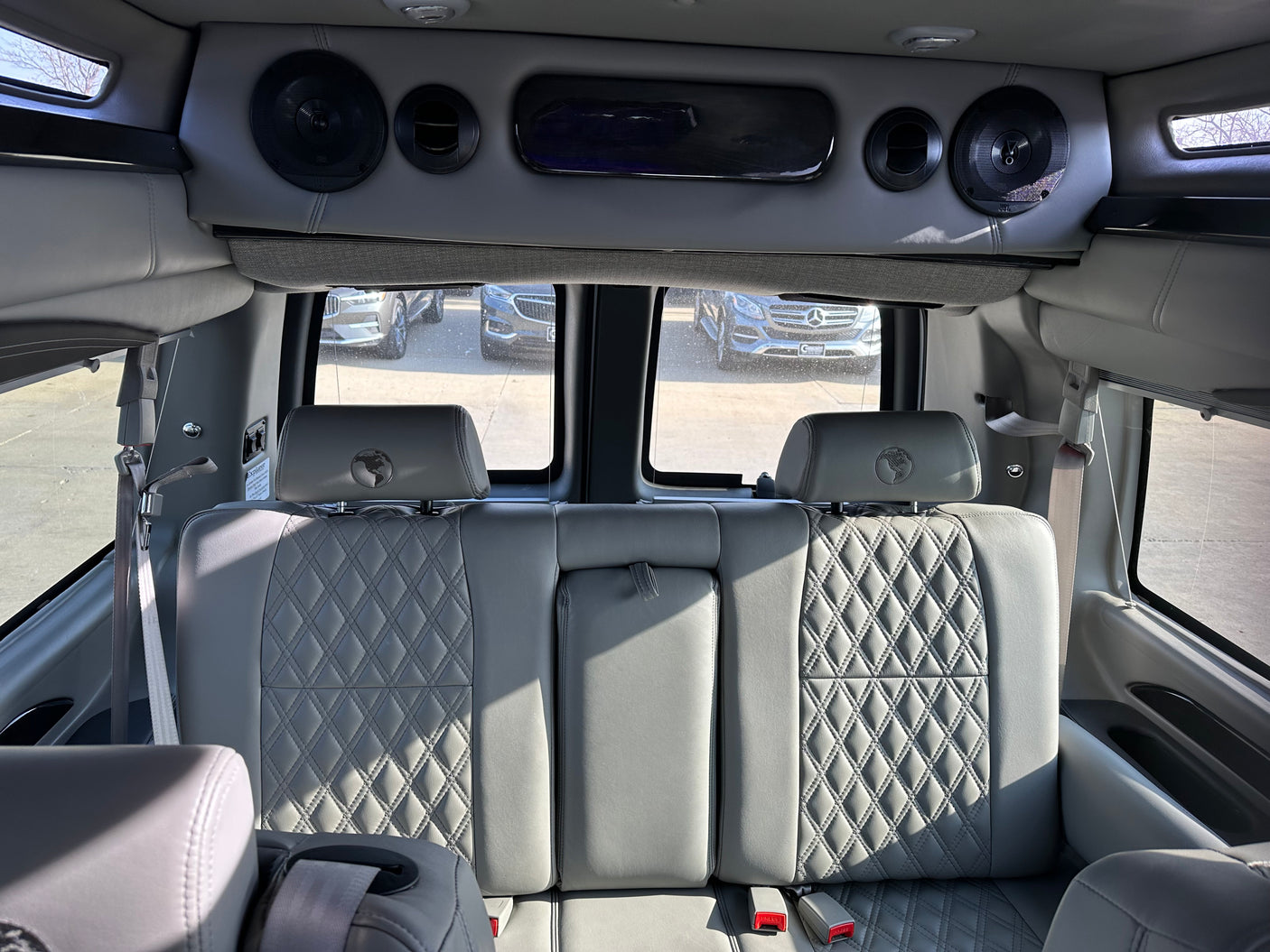 Luxury RV rental: detailed view of plush, grey quilted rear seats with globe emblems & overhead console with speakers.