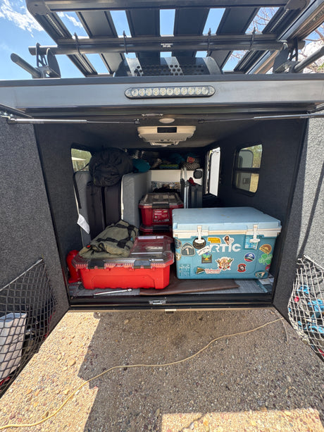 Organized rv rental camper rear storage area, featuring an RTIC cooler, gear, and Husky bins for road trips.
