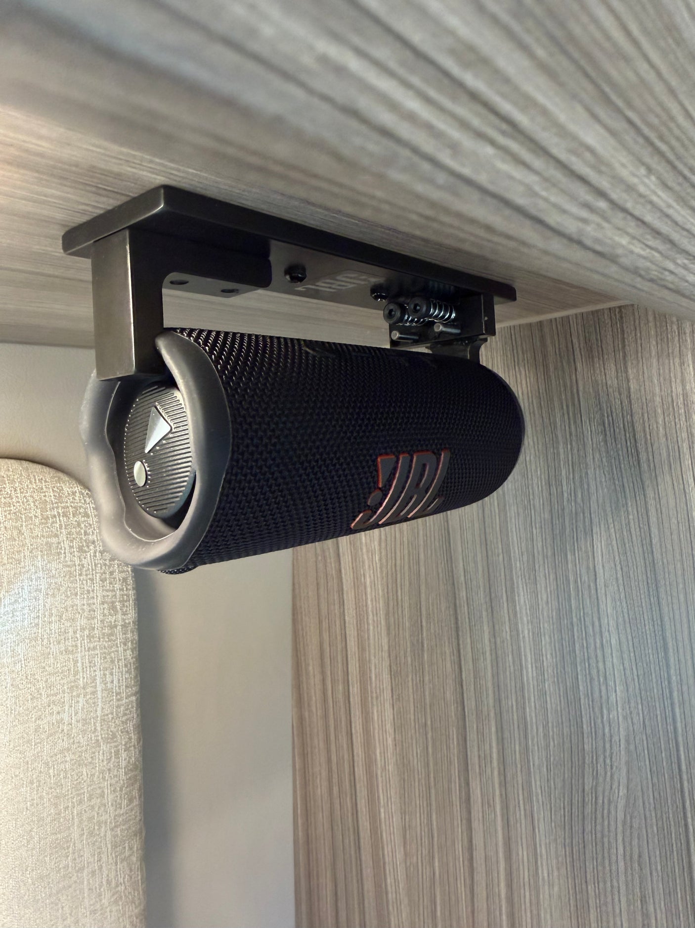 A black JBL portable speaker is securely mounted beneath a light wood-grained cabinet in an RV rental interior.