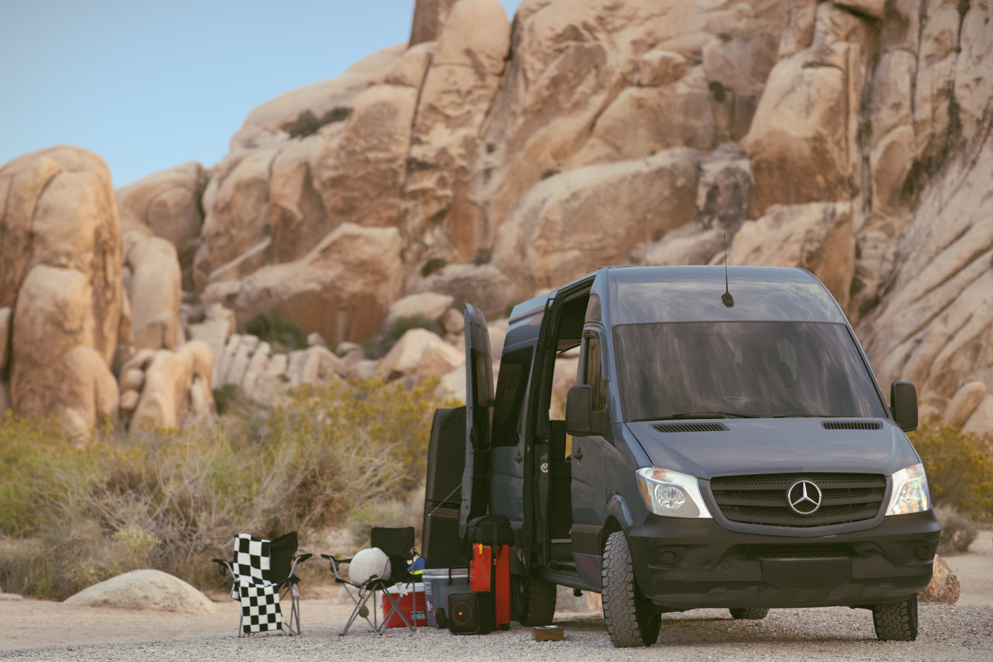 RV rental adventure: Mercedes Sprinter van camping in a desert landscape with large rock formations and gear.