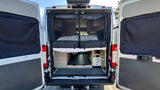 Explore this RV rental! Open rear van doors reveal a cozy bed, organized storage, and utility panel, protected by an insect screen.