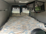 Cozy RV rental sleeping area features patterned bedding, pillows, and hanging storage.