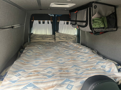 Cozy RV rental sleeping area features patterned bedding, pillows, and hanging storage.