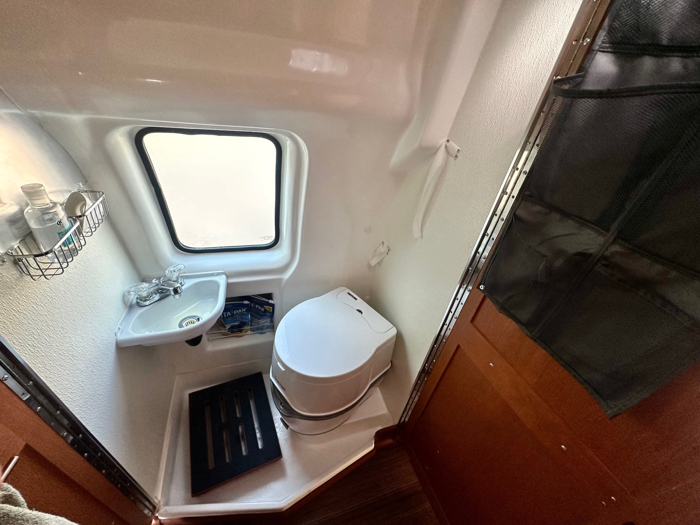 This rv rental's compact bathroom features a corner sink, Thetford Porta Potti toilet, window, and storage. — photo 10