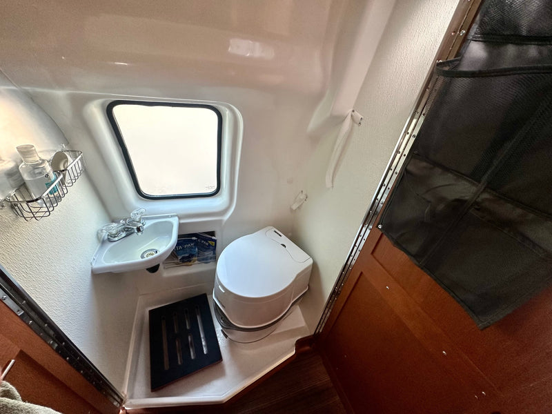 This rv rental's compact bathroom features a corner sink, Thetford Porta Potti toilet, window, and storage. — photo 10