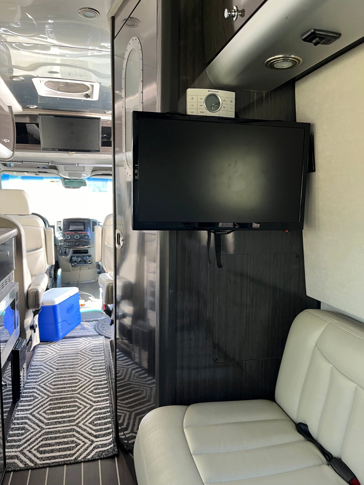 Inside a modern RV rental: sleek interior with TV, Dometic controls, comfortable seating, and a patterned rug.