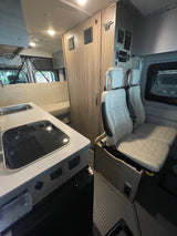 Interior view of an RV rental camper van featuring a compact kitchen, passenger seats, and rear bench seating for comfortable travel.