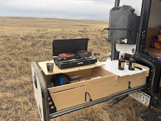  parked on dirt with mountains in the background. Ready for off-road camping.|RV rental: Rear platform with a cooler and open storage box. Perfect for your outdoor adventure gear.|Close-up of a white TigerMoth Overland Edition off-road camper — photo 6