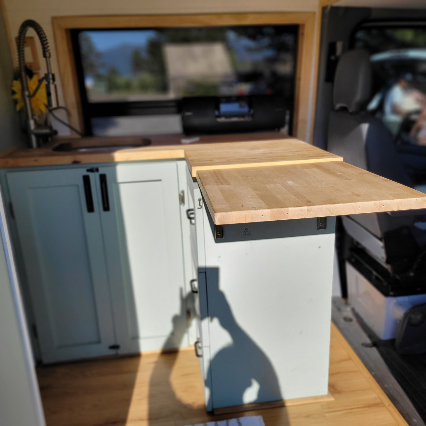 RV rental's cozy camper van interior with a light wood kitchen featuring a sink, pull-out faucet, and extendable wooden countertop.