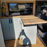 RV rental's cozy camper van interior with a light wood kitchen featuring a sink, pull-out faucet, and extendable wooden countertop.