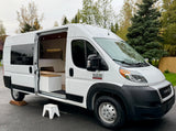 White Ram ProMaster camper van, ideal for rv rental. Open door reveals a cozy, custom-built interior with a bed & lighting.