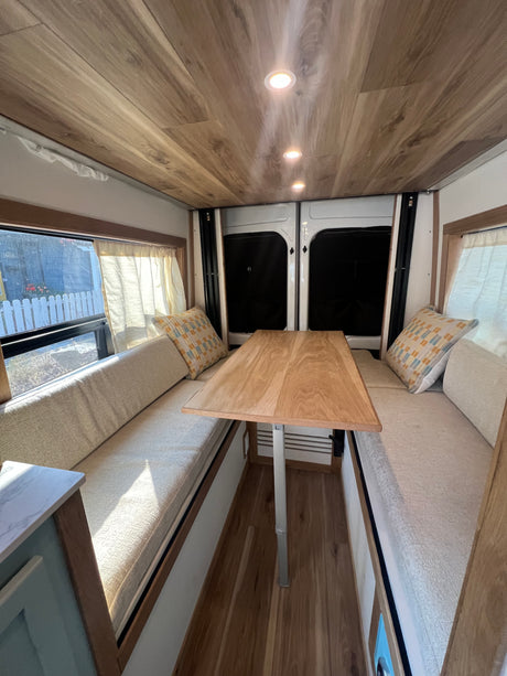 Cozy RV rental campervan interior: bench seating, wooden table, warm lighting, and a small counter. Ready for your travels!