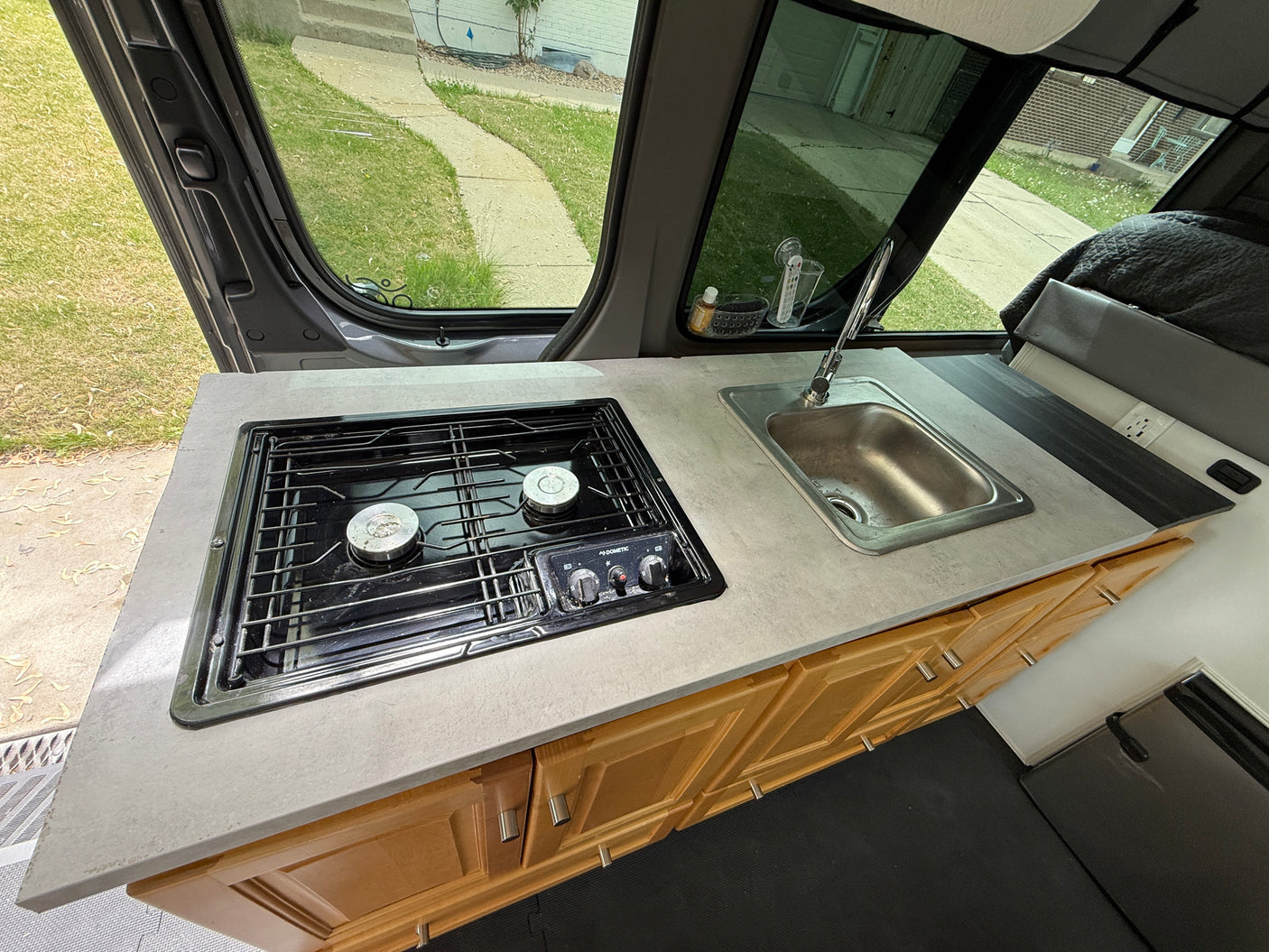 RV rental interior: A functional kitchen with Dometic stove, stainless steel sink, wood cabinets, and street view.