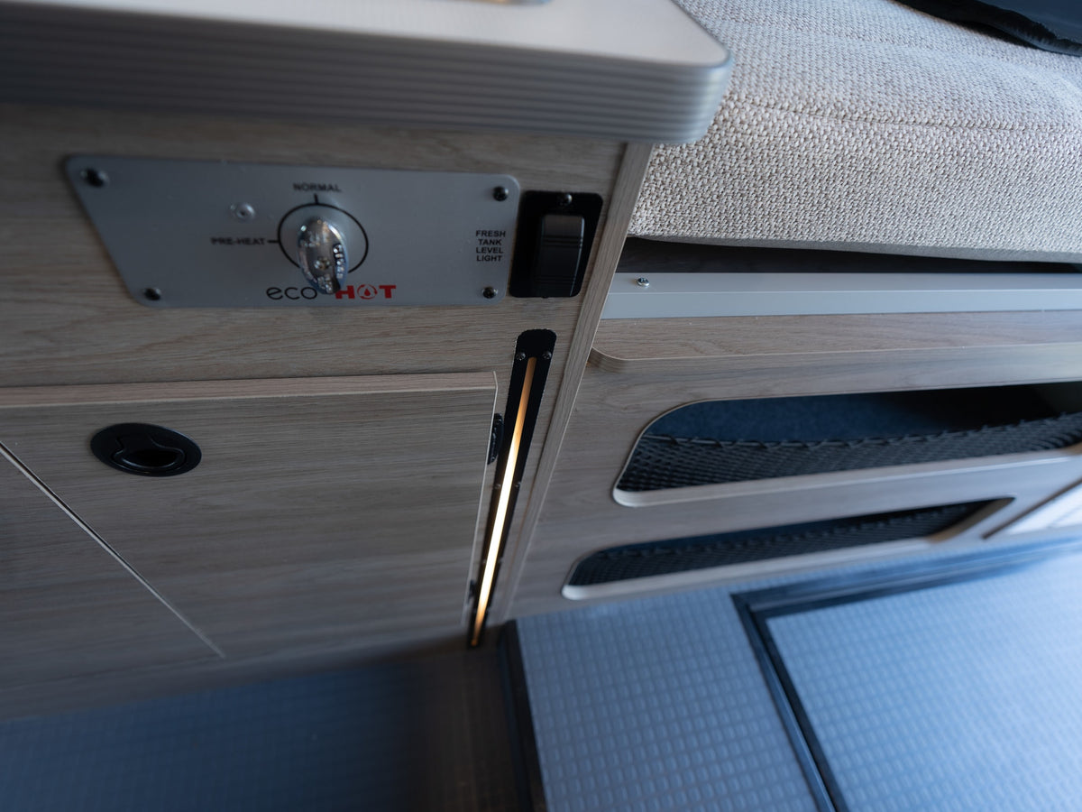 Control panel for an ecoHOT water heater, fresh tank light, and storage nets inside an RV rental. LED lighting illuminates. — photo 15