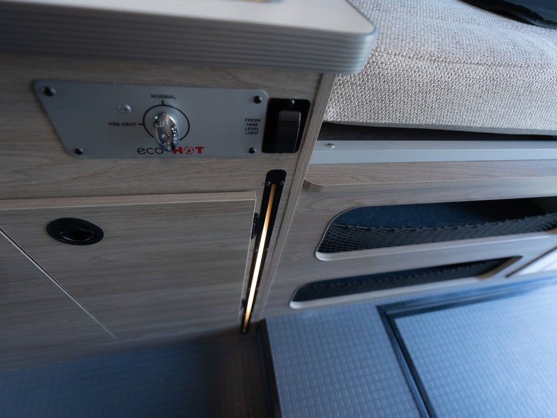 Control panel for an ecoHOT water heater, fresh tank light, and storage nets inside an RV rental. LED lighting illuminates. — photo 15