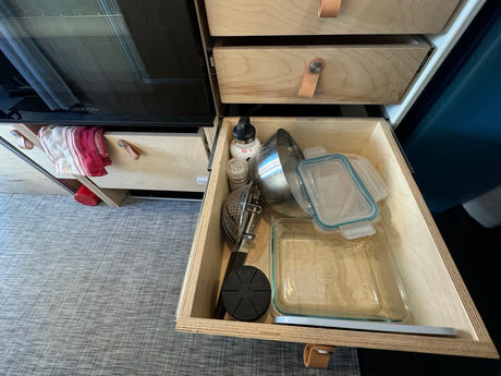 Efficient RV rental kitchen storage with pull-out drawers, showing various cooking essentials and glass containers.