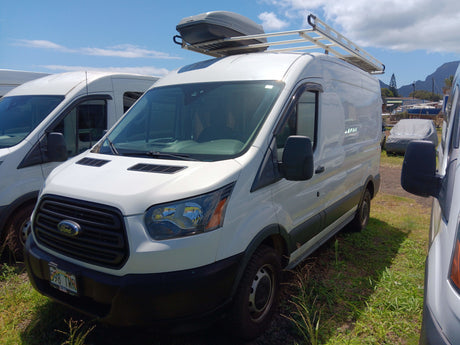Front view of a white Ford Transit van, set up as an RV rental, with a roof cargo box and ladder rack. Parked in a sunny outdoor lot.