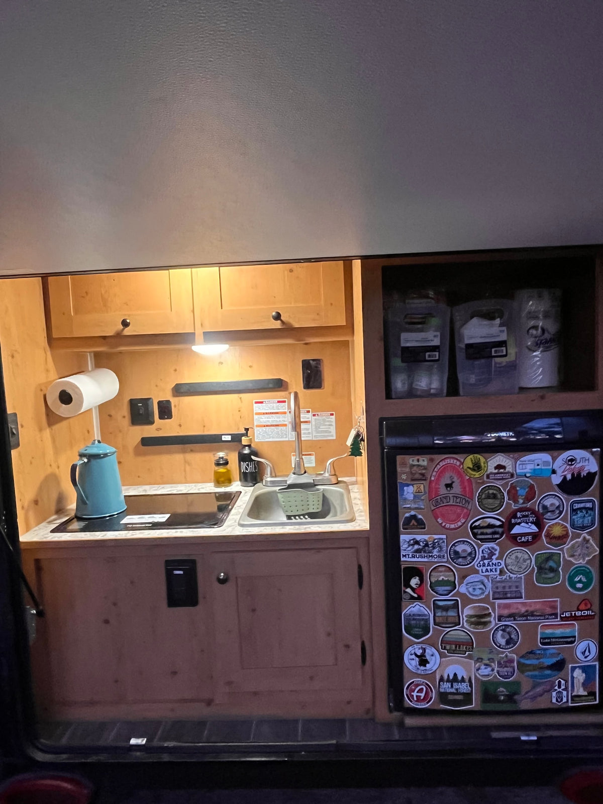RV rental kitchen: functional space with a sink, stovetop, and a fridge adorned with diverse travel stickers. — photo 13