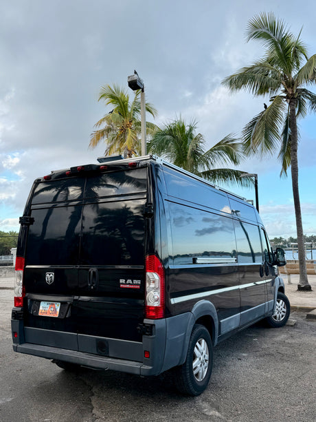 A black Ram ProMaster RV rental with a Utah plate, parked under palm trees on a cloudy day, ready for adventure.