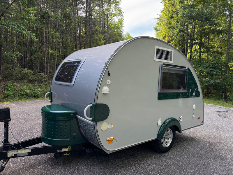 Grey & green teardrop RV rental parked on an asphalt road in a green forest, ready for travel. — photo 3