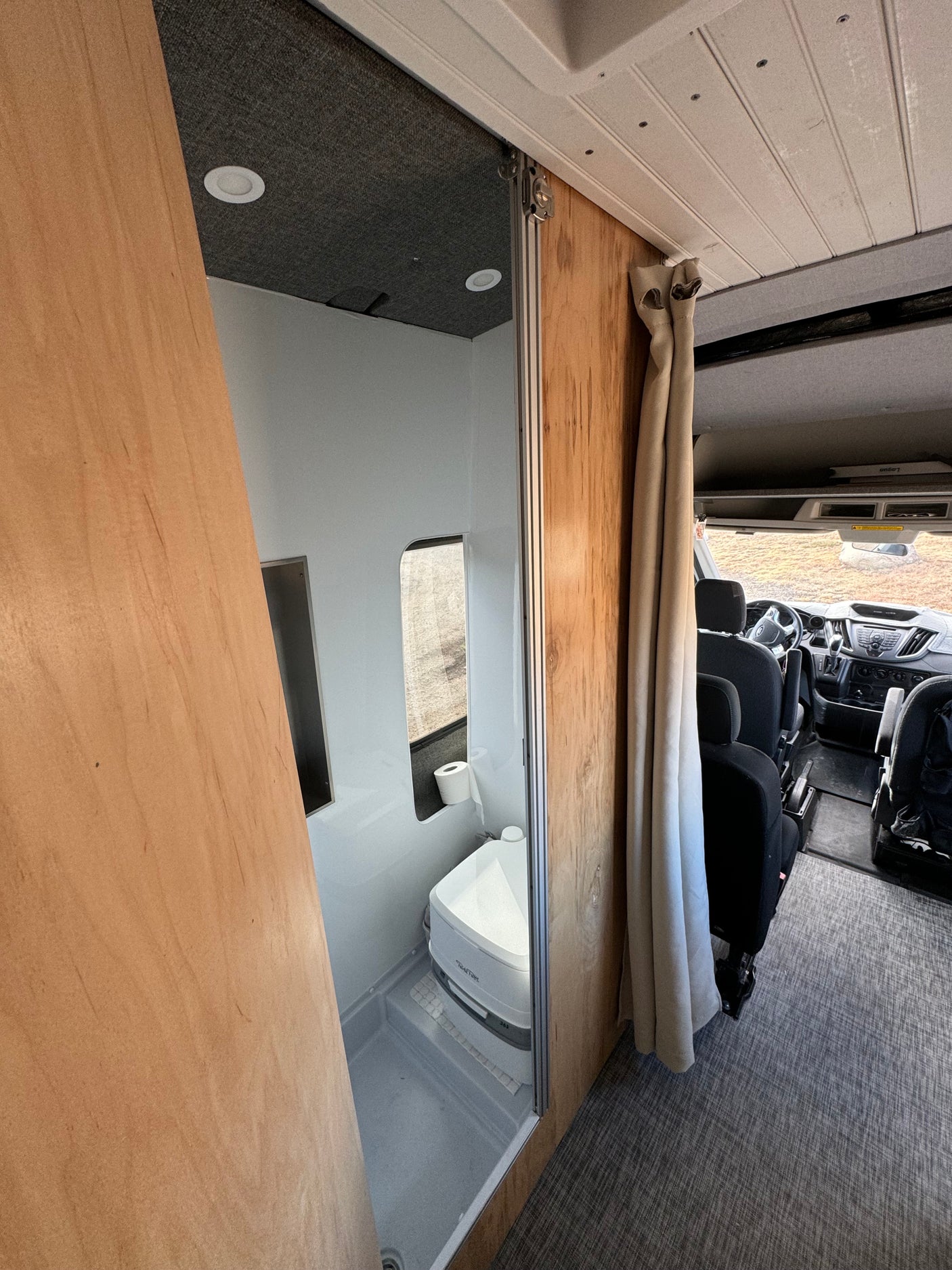 RV rental interior: A compact bathroom with toilet and shower is on the left, leading to the front cab area.