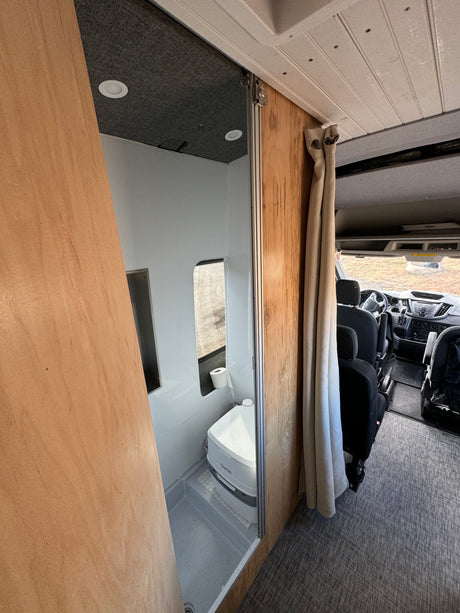 RV rental interior: A compact bathroom with toilet and shower is on the left, leading to the front cab area.