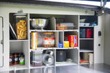 Organized RV rental kitchen pantry with shelves holding pasta, snacks, spices, cooking tools, and supplies for camping.
