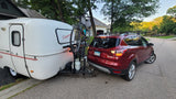 A red SUV tows a white Scamp travel trailer RV rental with a bike, ready for outdoor adventures.