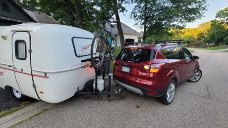 A red SUV tows a white Scamp travel trailer RV rental with a bike, ready for outdoor adventures.
