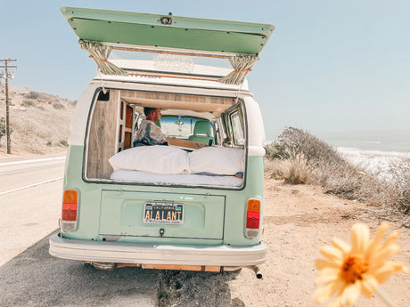 This mint green RV rental, a classic VW van, is parked with its hatch open, offering a bed and ocean view.