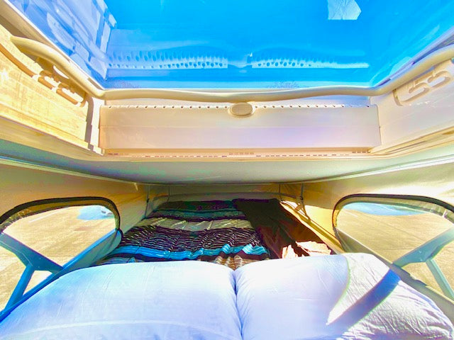 Inside an RV rental: a comfortable bed under a clear pop-top roof, offering sky views. Ready for adventure.