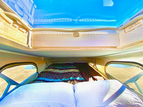 Inside an RV rental: a comfortable bed under a clear pop-top roof, offering sky views. Ready for adventure.