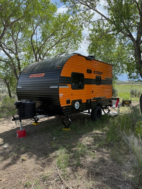 An orange & black compact RV rental sits leveled in a shady campsite