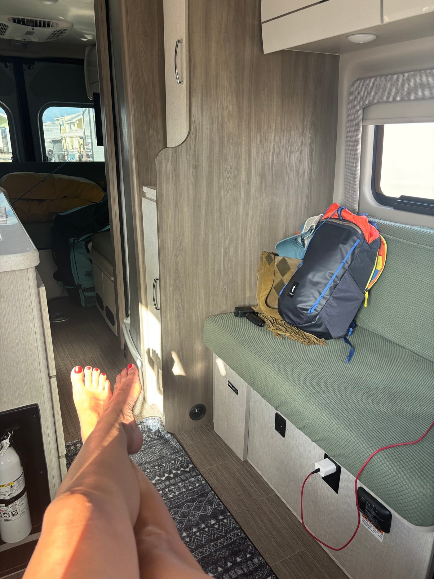 Sun-drenched RV rental interior with bare feet, green seating, storage, and a charging station. Ideal for travel comfort. — photo 8