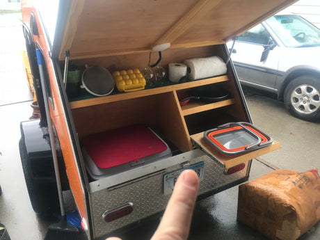 RV rental: Teardrop trailer's rear galley kitchen, organized with camping cookware, paper goods, and a pull-out shelf.