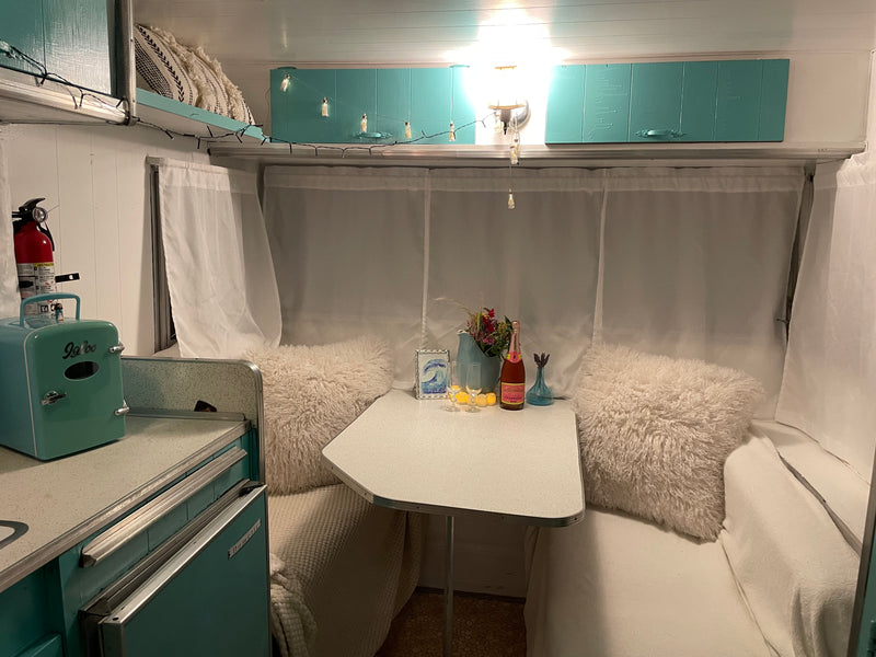 Cozy retro RV rental interior featuring a dining nook, teal accents, and a champagne setup for a charming getaway. — photo 7