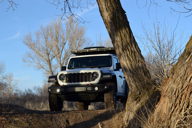 Adventure-ready white Jeep Rubicon with a rooftop tent, perfect for an RV rental escape, parked on a dirt path.