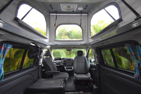 Inside a comfortable rv rental camper van: pop-top, front seats, and lush tropical views for your next adventure.