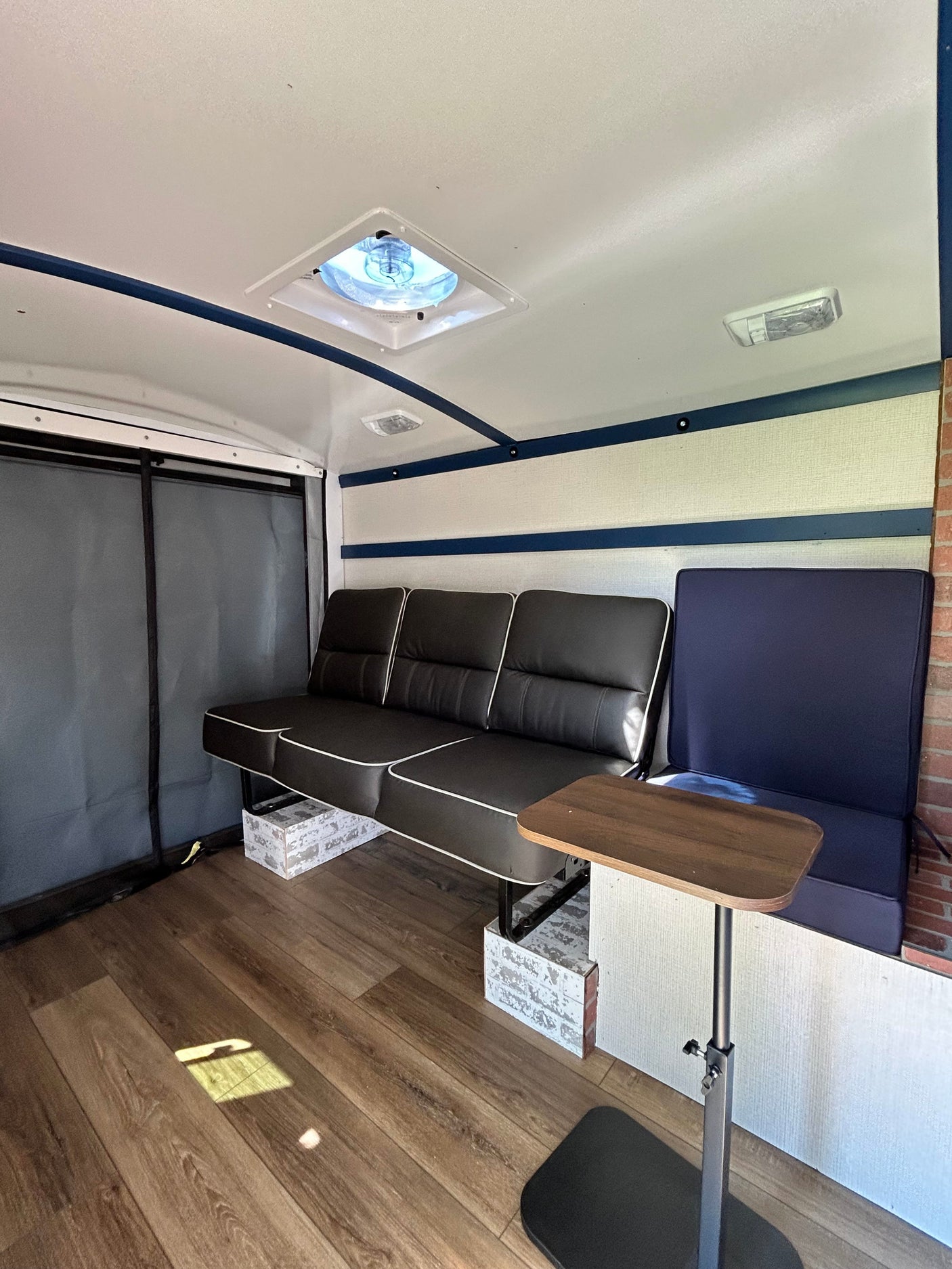 Step inside this rv rental's modern interior, featuring a black sofa, blue seating, wood-look floor, and adjustable table.
