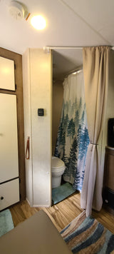 RV rental bathroom showing toilet, forest shower curtain, wood floor. RV interior features include a light & smoke detector.