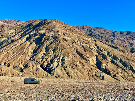 RV rental: A grey camper van on a vast, rocky desert floor under a clear sky, backed by arid mountains.