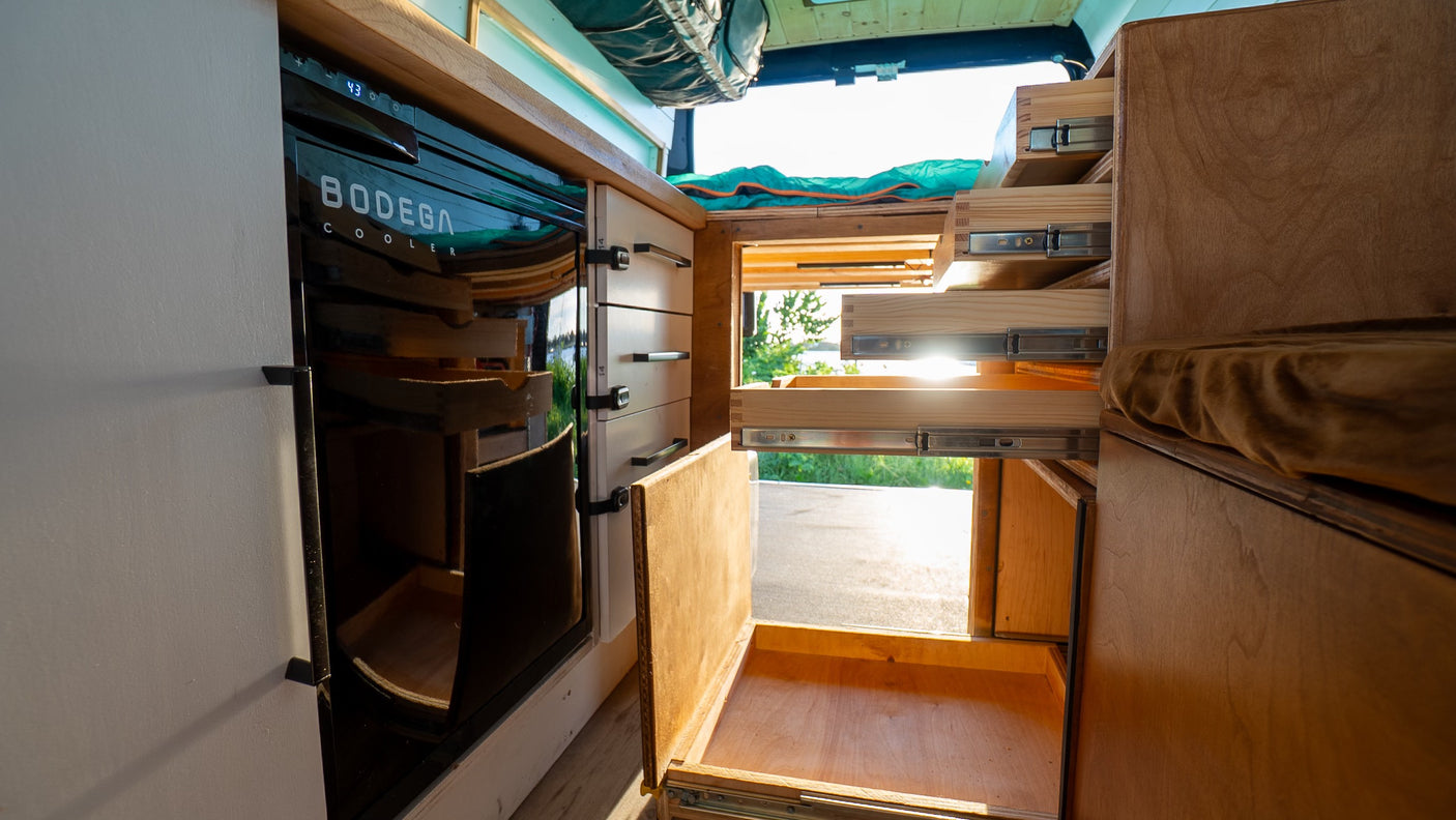 Inside an RV rental, discover smart storage: pull-out drawers, a BODEGA cooler, and custom wooden cabinetry.