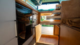 Inside an RV rental, discover smart storage: pull-out drawers, a BODEGA cooler, and custom wooden cabinetry.