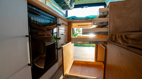 Inside an RV rental, discover smart storage: pull-out drawers, a BODEGA cooler, and custom wooden cabinetry.