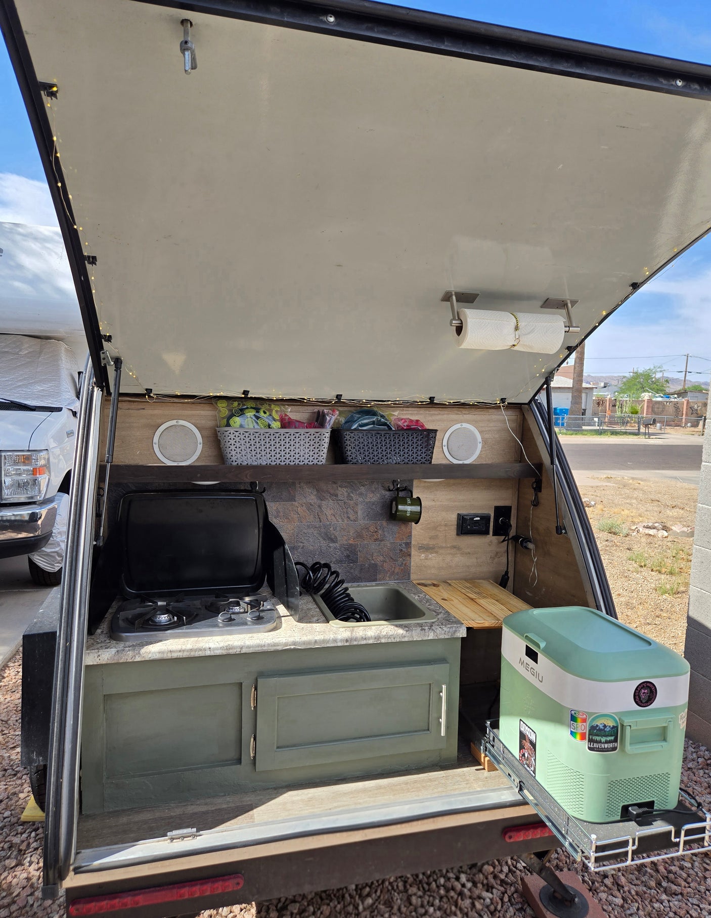 This organized teardrop RV rental's outdoor kitchen features a stove, sink, speakers, and a convenient pull-out cooler for camping.